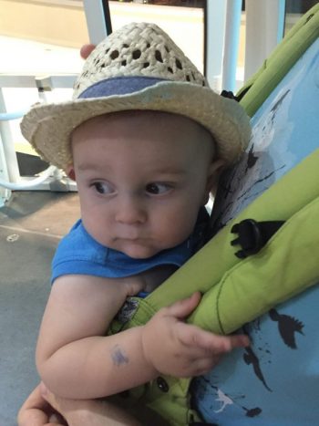 baby boy in a hat holding onto the straps of a green baby carrier