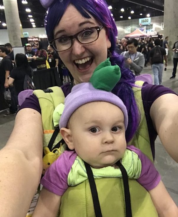 a baby and mom in my little pony cosplay at a convention, held in a green Lillebaby baby carrier