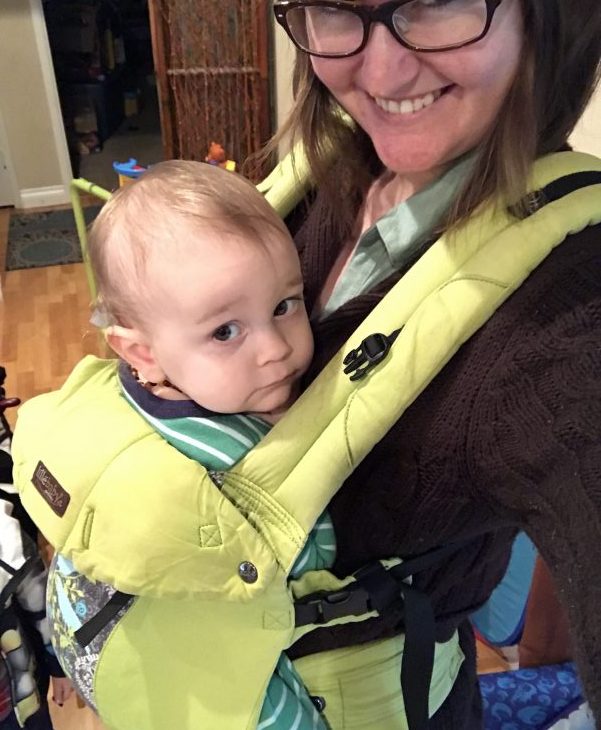 A baby seated in a green Lillebaby carrier, worn by his mom