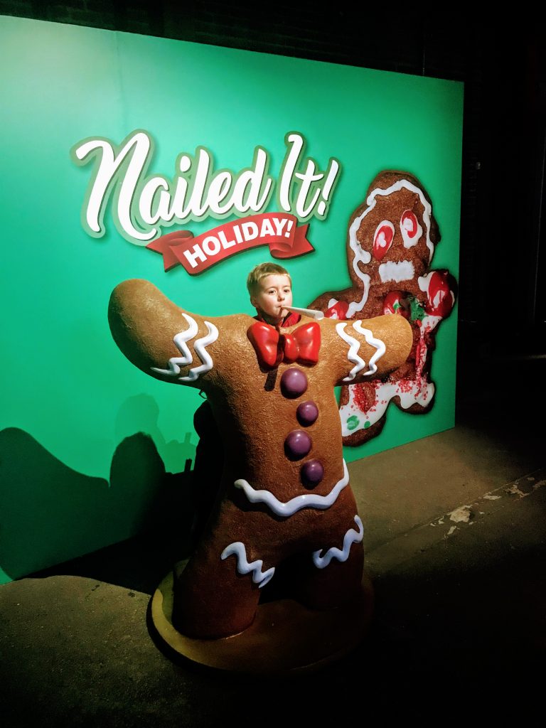 Brendan poses behind a giant gingerbread cookie photo opp at the Nailed It Holiday village