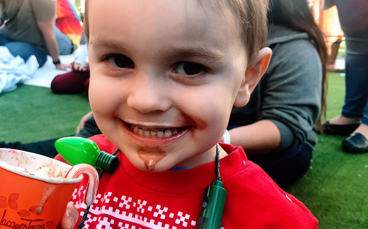 A little boy drinks hot chocolate, with chocolate all over his face