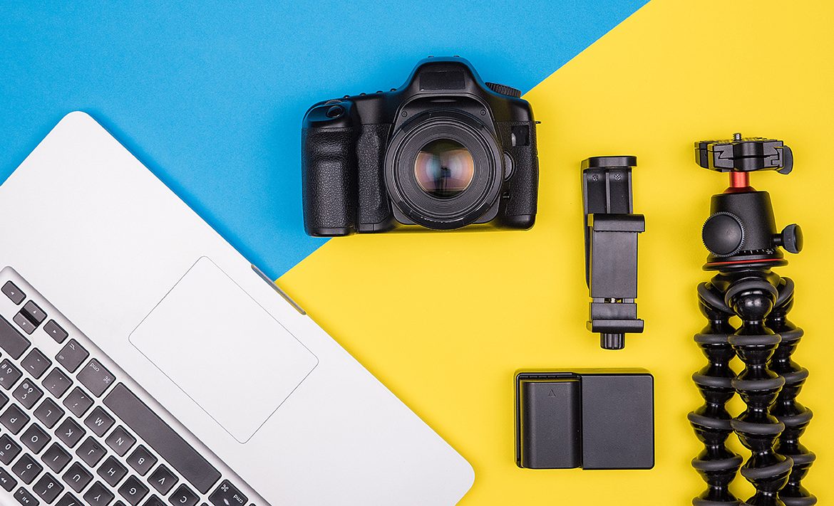 Camera with accessories next to a laptop on two colored background. Top view. Flat lay