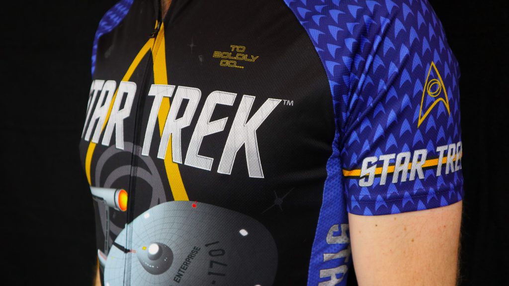 Closeup of a blue Star Trek cycling jersey featuring the Enterprise and delta logo, part of the fitness apparel line from Brainstorm Gear