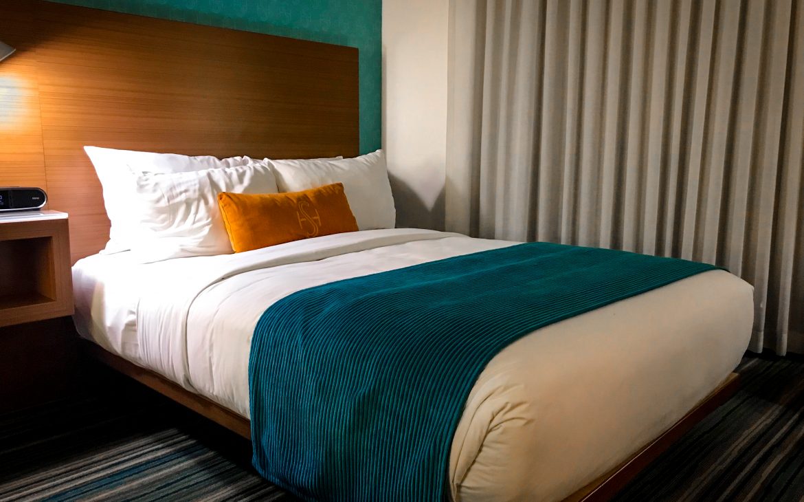 Double size bed with turquoise duvet cover and orange pillow at the Shore Hotel Santa Monica