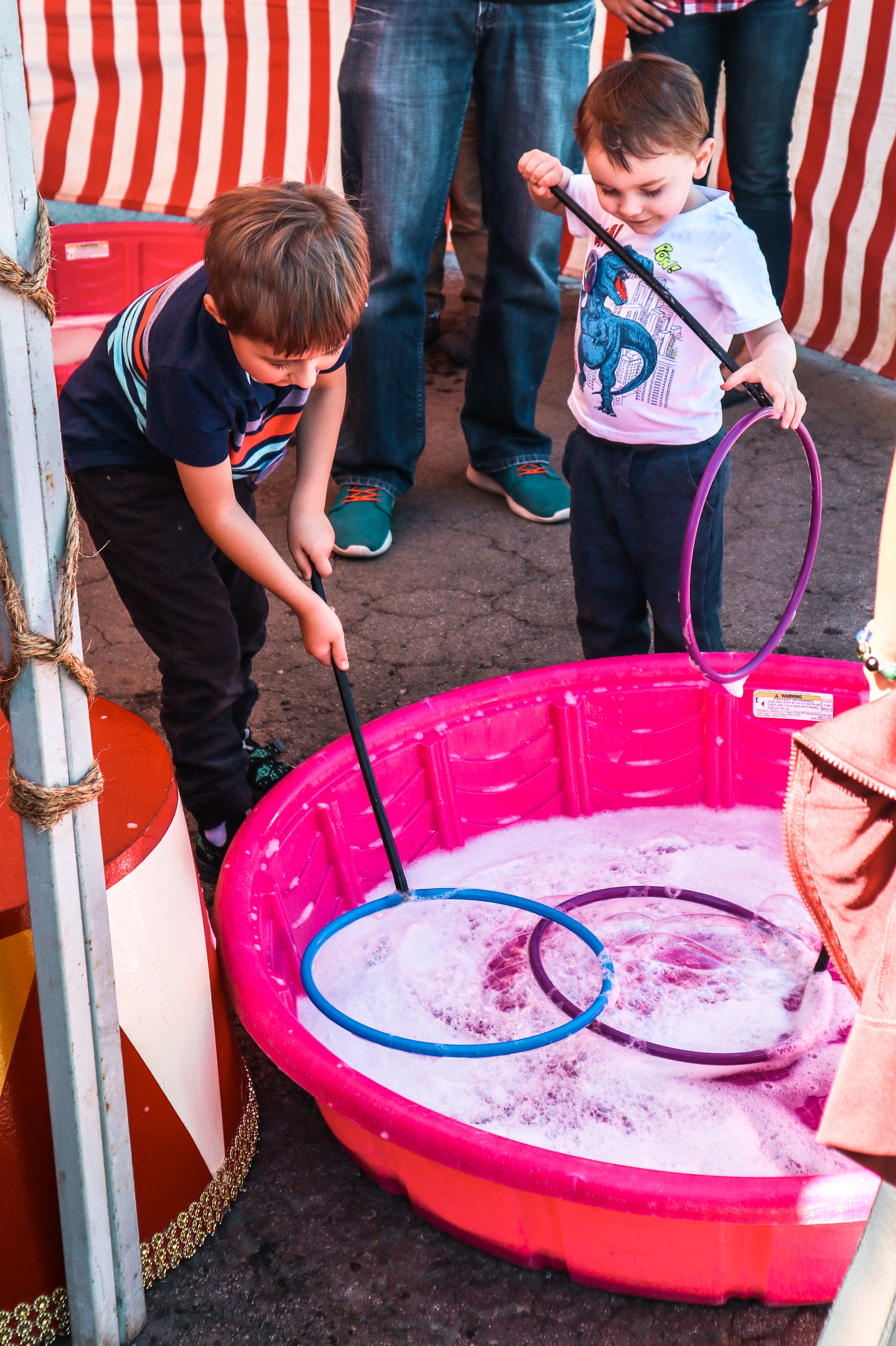 two little boys creating giant bubbles with wands in a red and white striped circus tent
