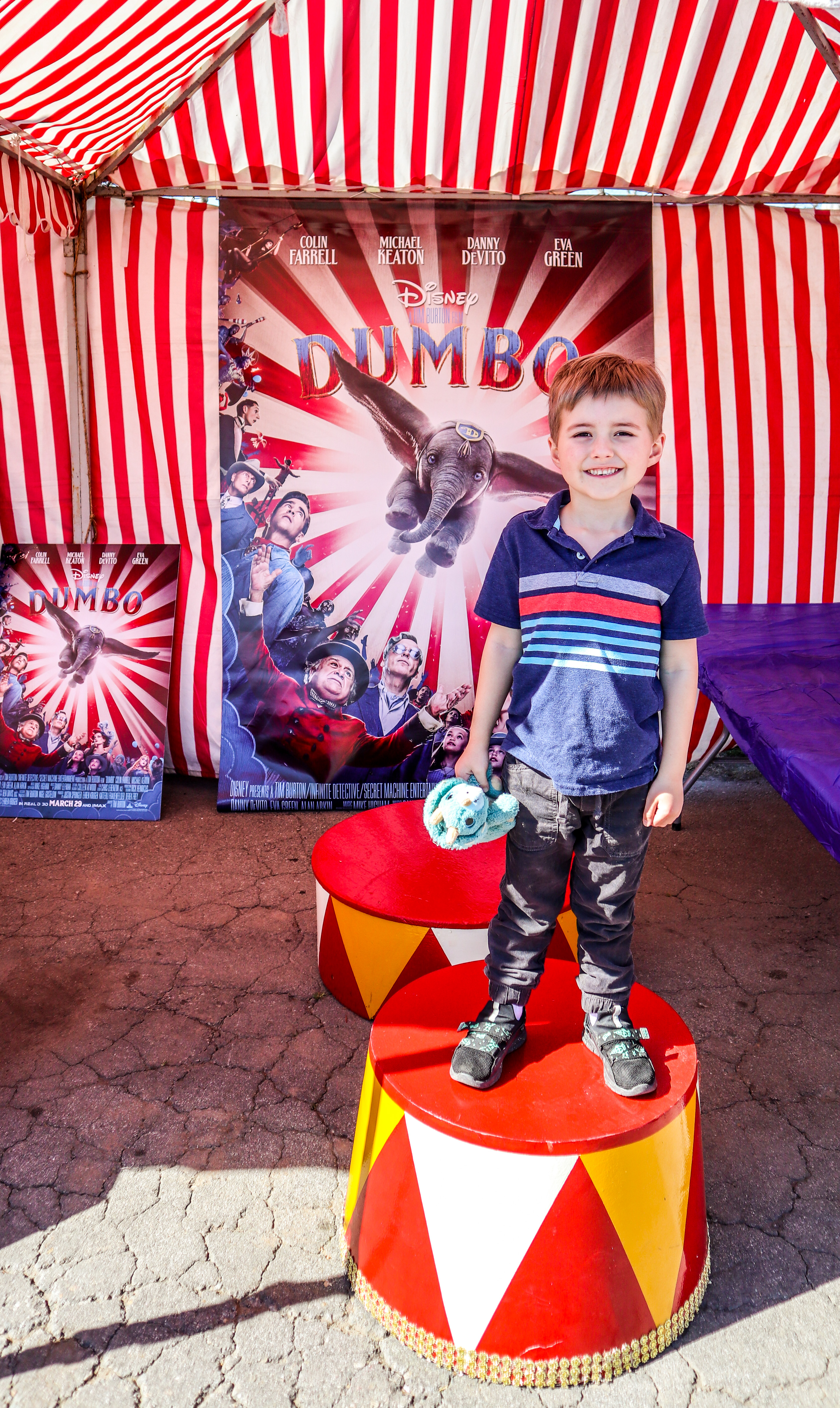 A boy smiles in front of a Disney Dumbo poster at the Dumbo promotional booth at STEA2M Fair