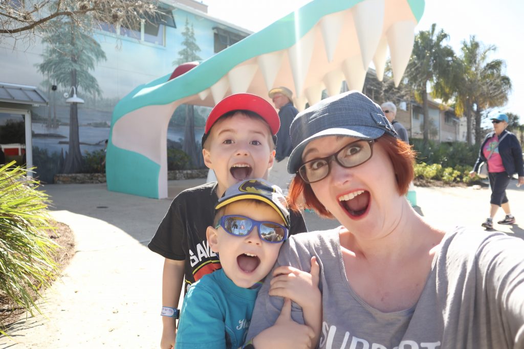 Mom with two little boys poses in front of the Gatorland teeth statue, acting scared