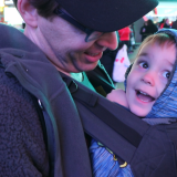 a happy little boy rides in his dad's Lillebaby baby carrier, looking at the lights of Times Square in New York City