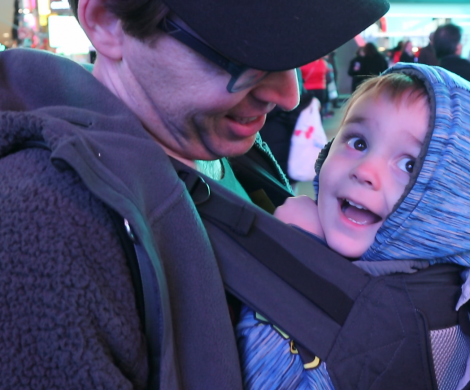 a happy little boy rides in his dad's Lillebaby baby carrier, looking at the lights of Times Square in New York City