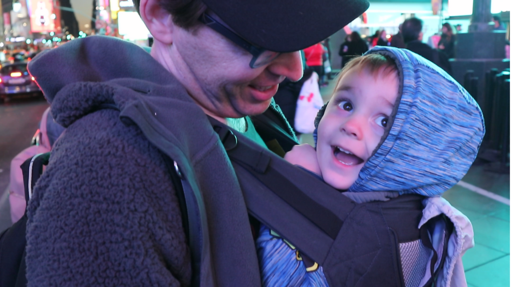 a happy little boy rides in his dad's Lillebaby baby carrier, looking at the lights of Times Square in New York City