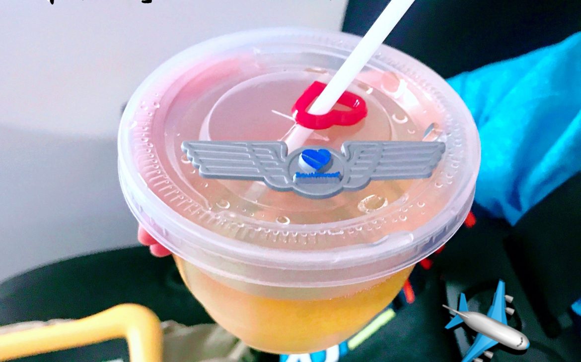 A pair of flight wings and a heart attached to the top of a cup of apple juice on an airplane. A little boy is holding the cup. Caption says "Why we love Southwest"