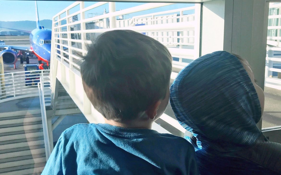 Two young kids look out a window at the airport terminal