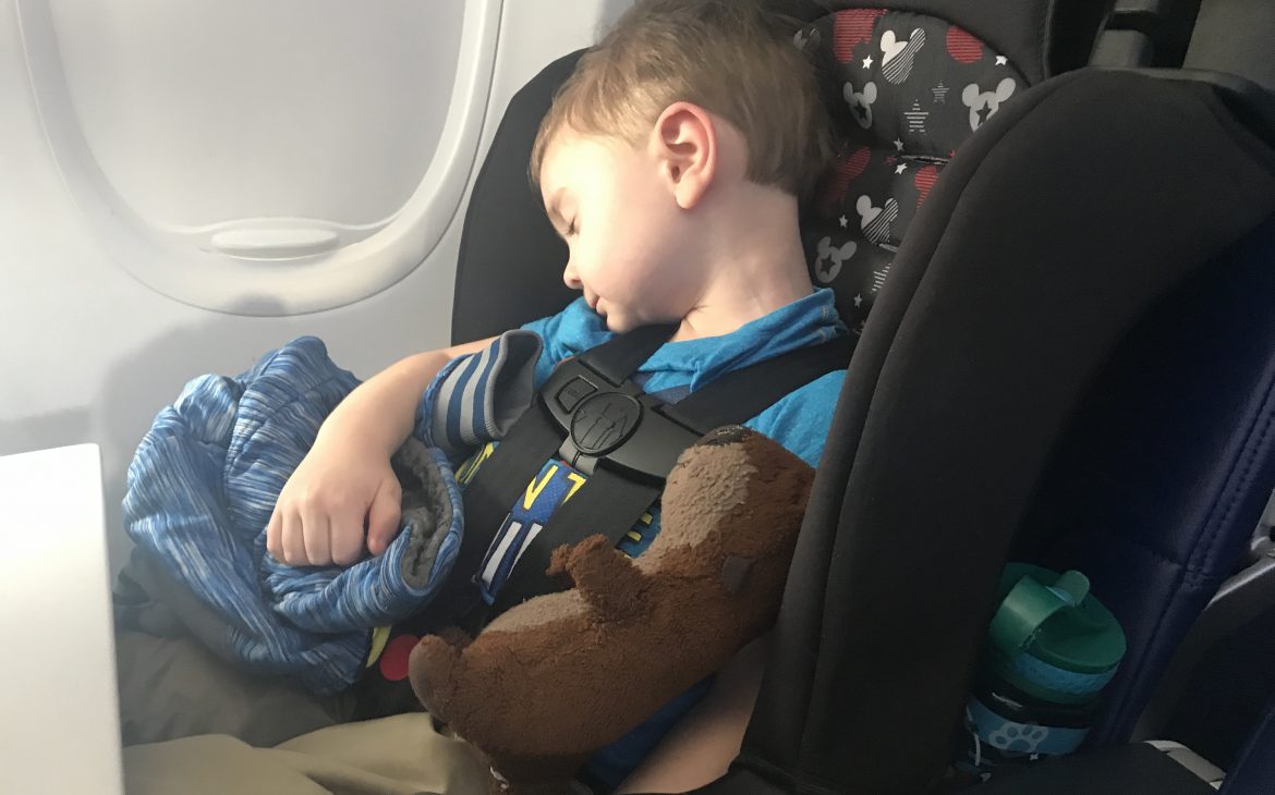 A little boy sleeps in his car seat on an airplane