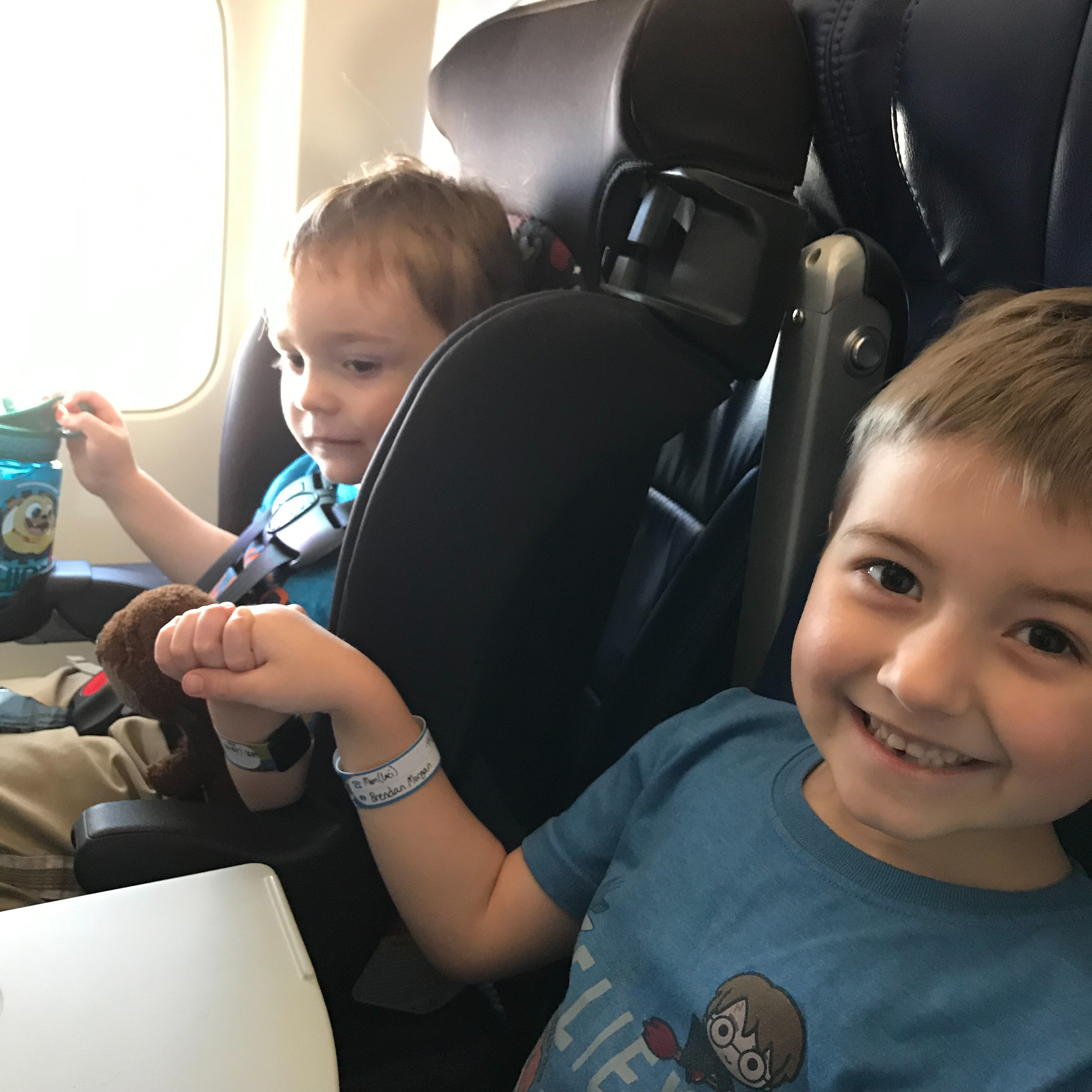 A kid holds his brother's hand on an airplane trip, flying with young kids