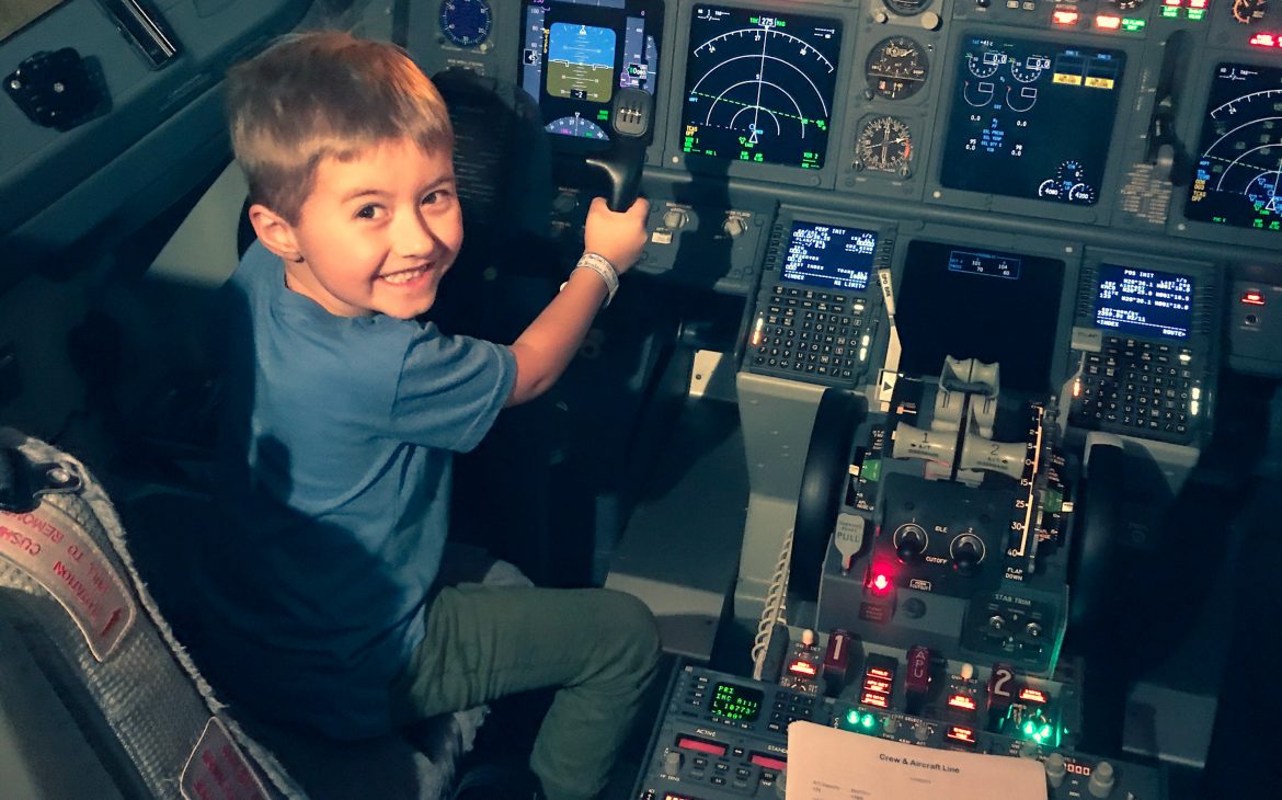 A happy little boy sitting in the pilot seat of a Southwest airplane, pretending to be the pilot