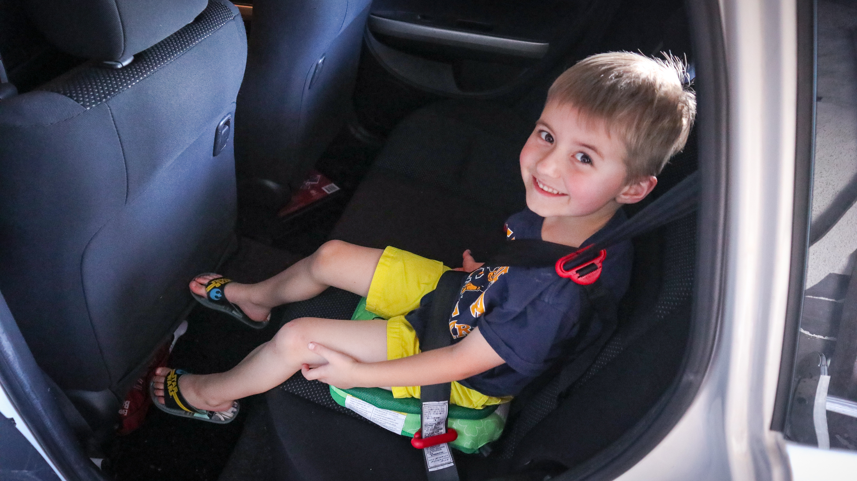 Six year old boy sitting in the back seat of a car, testing out the Bubblebum travel car seat