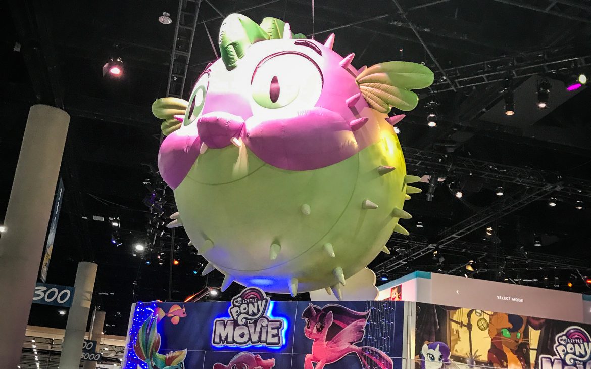 A large balloon of Spike the Dragon pufferfish above the My Little Pony booth in the exhibit hall of san diego comic con