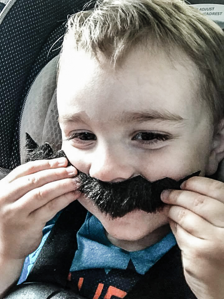 little boy holding up a fake Mario moustache